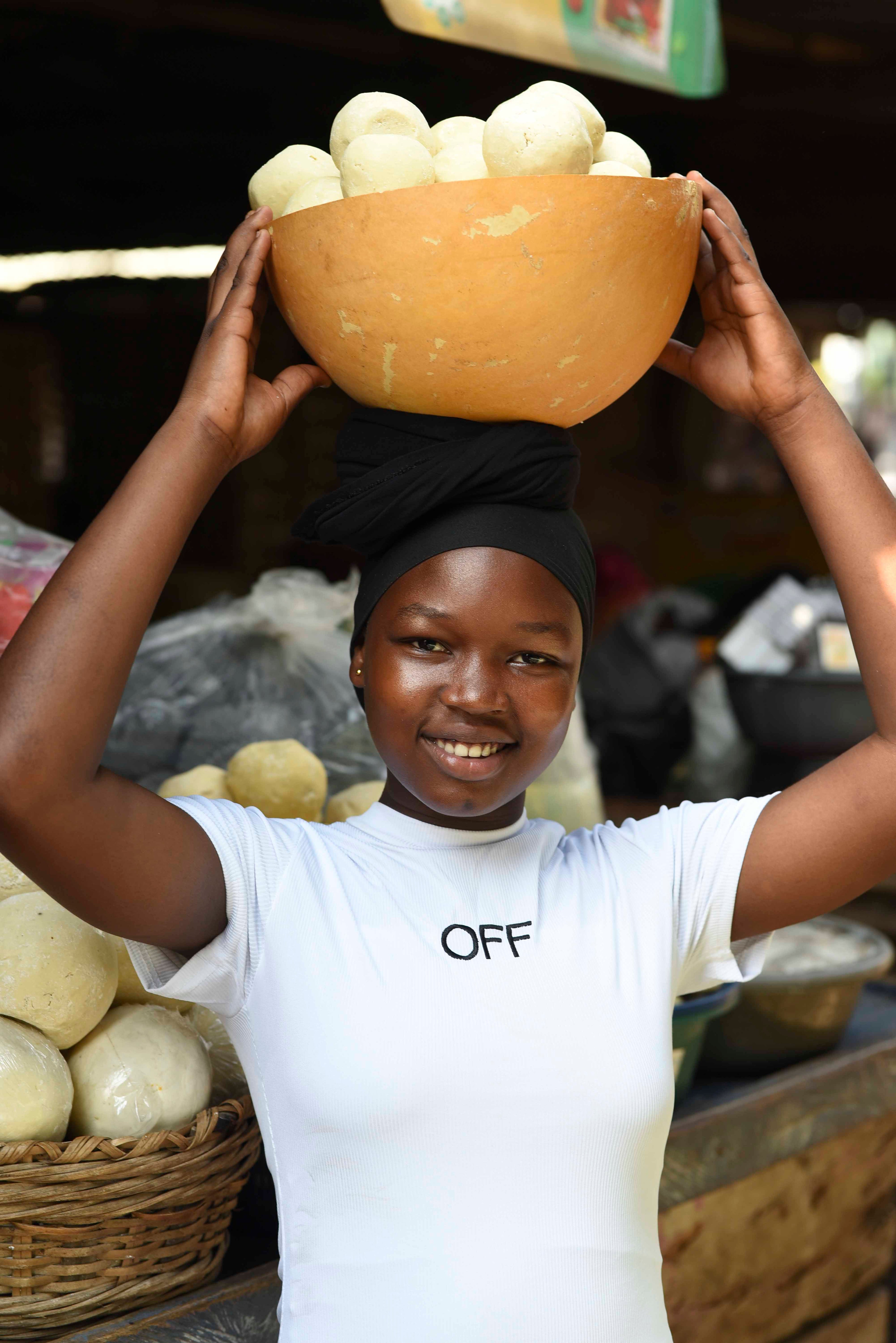 Woman carrying a calabash bowl of Shea Butter on her head in a Ghana market setting